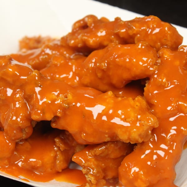 Pile of boneless chicken wings covered in shiny orange buffalo sauce on a white plate.