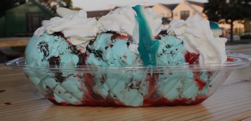 Blue ice cream sundae with chocolate chunks, red syrup, whipped cream, and a blue gummy shark.