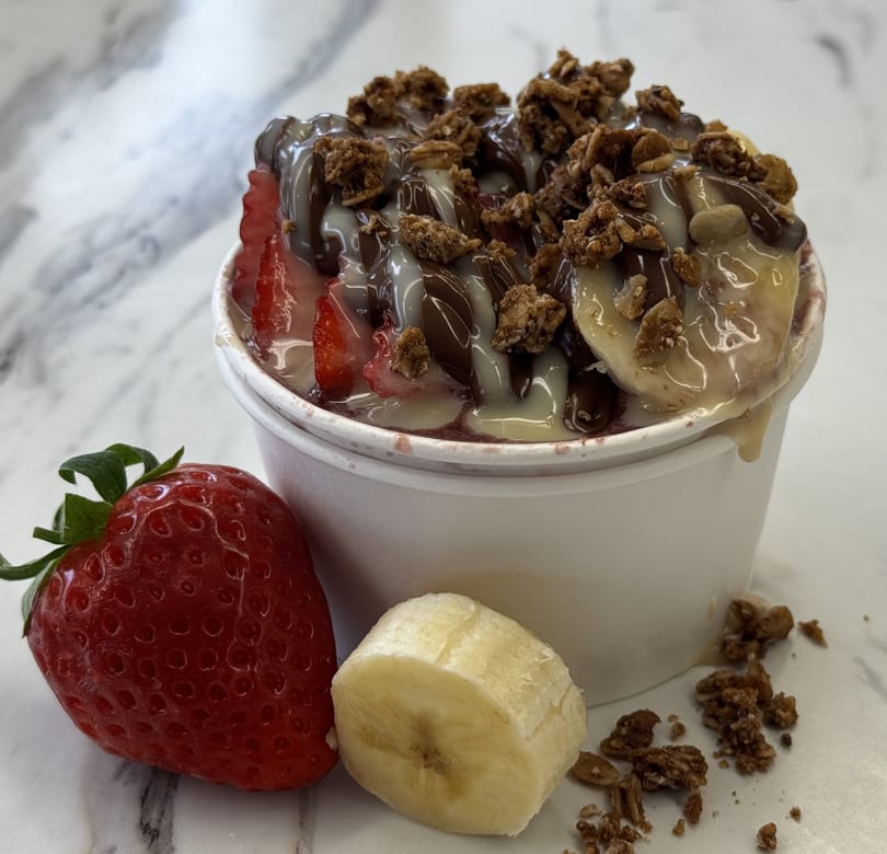 Delicious açaí bowl topped with fresh fruit, granola, and sweet drizzles on marble.