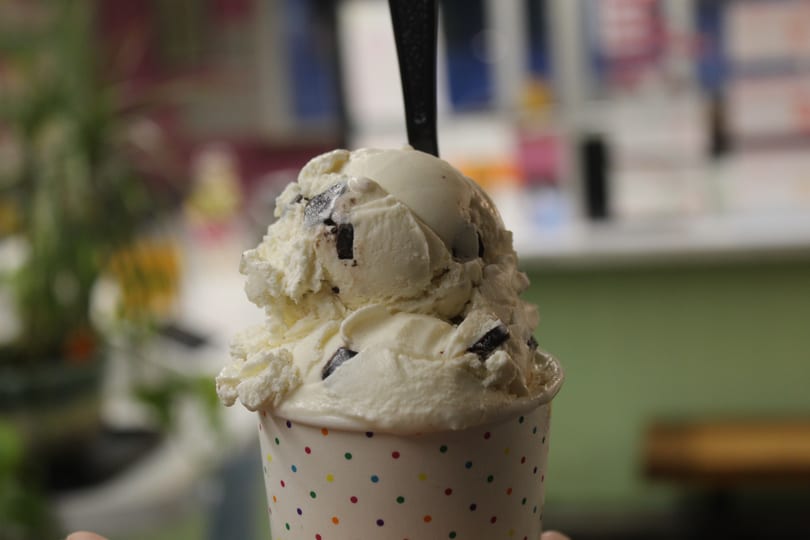 Close-up of chocolate chip ice cream in a white polka dot cup with a spoon.