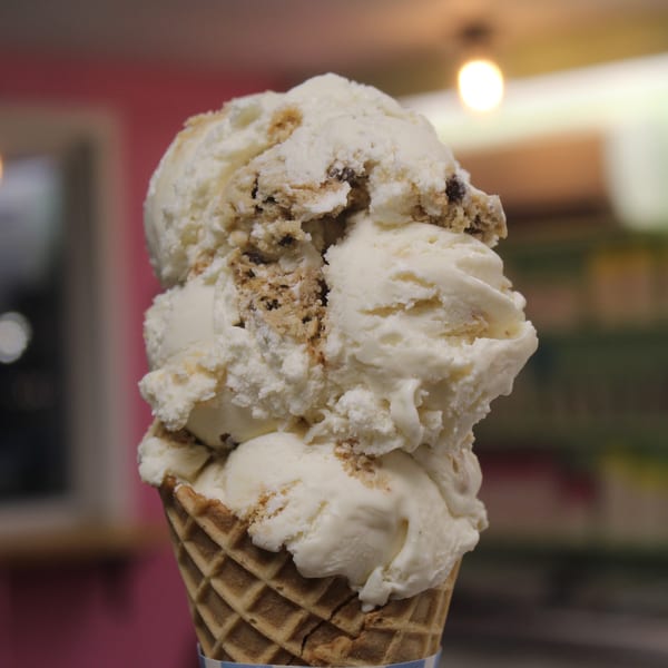 Multiple scoops of white ice cream with cookie chunks in a waffle cone.