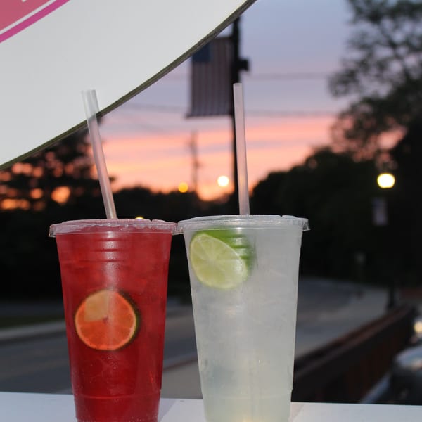 Two iced drinks, red and clear with lime, on a white surface at sunset.