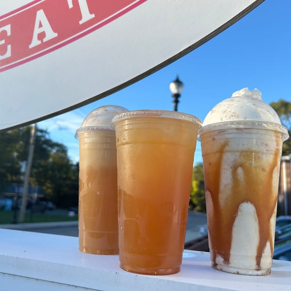 Three cold drinks, including iced tea and a caramel milkshake with whipped cream, on an outdoor ledge.