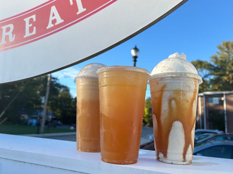 Three cold drinks, including iced tea and a caramel milkshake with whipped cream, on an outdoor ledge.