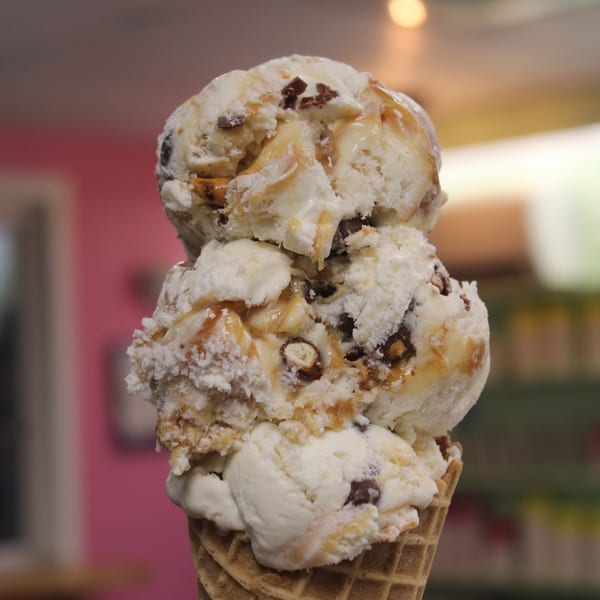 Three scoops of vanilla ice cream with chocolate and caramel in a waffle cone.