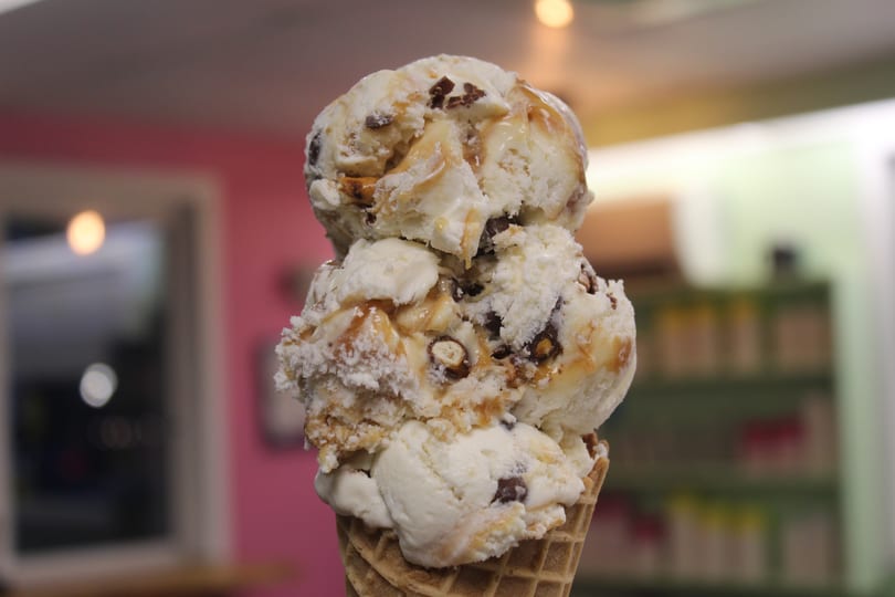 Three scoops of vanilla ice cream with chocolate and caramel in a waffle cone.