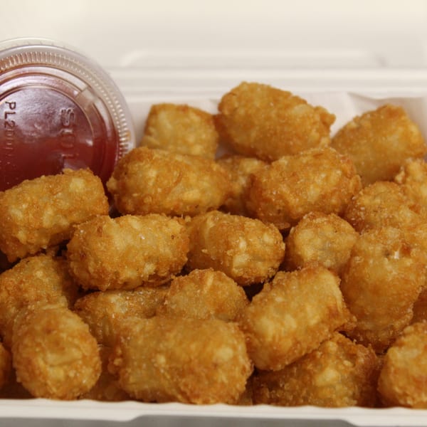 Crispy tater tots and a small cup of ketchup in a white takeout box.